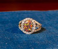 Front view of sterling silver ring with central opal-like CZ surrounded by smaller clear CZ stones, placed on blue fabric.