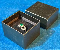 Ring in black jewelry box on blue fabric, showing overall presentation and box appearance.