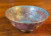 Angled side view showing the vibrant cloisonné enamel with bird and floral design inside the bowl on a wooden surface.