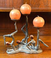 Front view of the solid metal Art Deco candle holder with three stylized figures holding round candles.