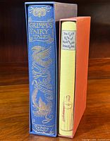 Two books in slipcases: Grimm's Fairy Tales in blue slipcase and Book of Humorous Anecdotes in orange slipcase.