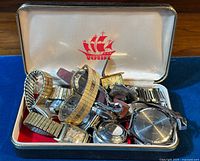 Tin box interior filled with a pile of metal-bracelet wristwatches in varied styles