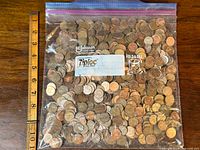 Top-down view of a large Ziploc bag containing hundreds of mostly Canadian pennies, with a ruler for size reference.