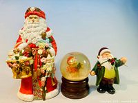 Full view of the large porcelain Belznickle Santa Claus figurine, the snowman snow globe, and smaller ceramic Santa figurine grouped together