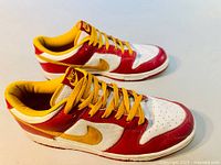 Side view of Nike Dunk Low sneakers showing red leather overlays, yellow Nike swoosh, white mesh, and yellow laces.