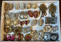 Top view of entire tray showing all 24 pairs of rhinestone and costume jewelry clip-on earrings with various designs and colors in a white box.