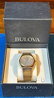 Bulova Accutron wristwatch in original box, showing gold-tone mesh bracelet and silver dial with date.