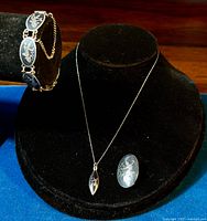 Photo showing bracelet displayed on a black bracelet stand, and pendant necklace and brooch displayed on a black necklace bust, showcasing the niello enamel details.