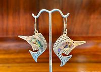 Pair of handcrafted sterling silver marlin swordfish earrings with abalone inlay on display stand, close-up showing detailed fish design and color.