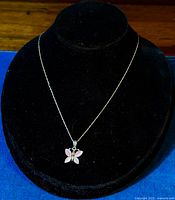 Full view of necklace displayed on a black stand showing the butterfly pendant with pink enamel.