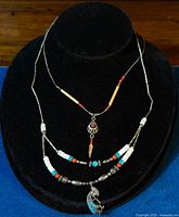 Full view of two vintage fetish necklaces displayed on black velvet stand showing beads and pendants.