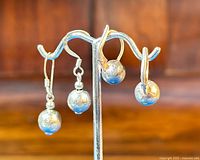 Two pairs of sterling silver ball earrings displayed on metal stand, showing different designs.