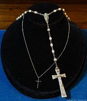 Full view of the silver rosary with oval beads and large crucifix alongside a smaller cross pendant on a separate silver chain.