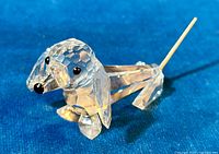 Clear faceted crystal dachshund dog figurine with coiled spring wire tail shown on blue fabric background.