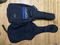 Top view of two black soft guitar cases, one with an external pocket with blue stripe and handle, the other plain with front zip.