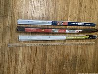 Three new door sweeps in packaging and one wooden yardstick on wooden floor.