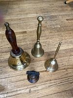 Four assorted bells on wooden floor, showing different sizes and handle styles.