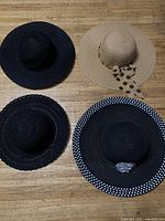 Four ladies' hats on wooden floor, showing two black lace hats and one beige hat with polka dot accessory, and one black wide-brim hat with gray accent.