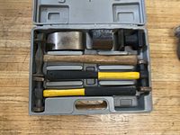 View of open plastic case showing two auto body hammers with yellow and black rubber handles, one hammer with wooden handle, and three various shaped metal dollies.