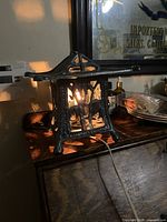 Side view of vintage brass lamp showing pagoda style roof and intricate cut-out sides with light on