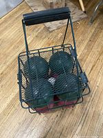 Top view of bocce balls inside black metal wire carrying cage on wood floor.