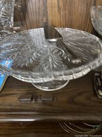 Glass cake stand with embossed leaf pattern and pedestal base, shown with matching cake knife placed on it.