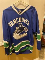 Front view of blue Vancouver Canucks hockey jersey with orca logo and 'Vancouver' text.