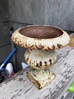 Side view of small cast iron planter showing fluted bowl with worn white paint and rusty interior.