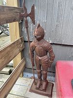 Front angled view of cast iron soldier guard figurine holding halberd, showing rust-colored surface and detailed armor.