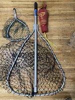 Two fishing nets and an E-Z Toss heaving line in a red carry bag placed on wooden floor.