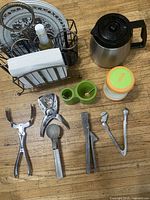 Overview of all items including coffee pot, plates, napkin holder with bottles, green container, orange-lidded jar, and metal utensils.