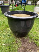 Front-side angle view of large black porcelain flower pot outdoors on grass, showing round shape and flared rim.