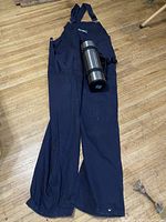 Full view of the navy blue coveralls laid flat on floor with the stainless steel Thermos placed on top.