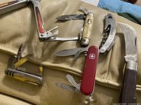 Photo showing the six cutting utensils including Swiss Army knives, Klein Tools multi-tool, and others arranged on a beige surface.