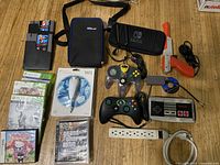 Wide view of Nintendo and Wii gaming items including games, controllers, carrying case, and accessories laid on a wooden floor.