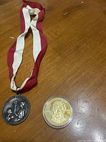 Photo showing the silver Olympic medal with red and white ribbon and the Princess Diana commemorative coin in protective case placed on wooden surface.