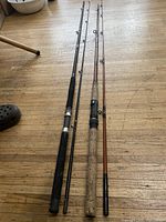Two fishing rods lying on wooden floor, showing full length with handles, guides and tips.