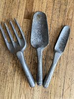 Set of three aluminum garden hand tools including a fork, shovel, and trowel laid on wooden surface.