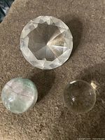 Photo showing three items: clear crystal ball, faceted glass stone, and polished stone sphere on brown surface.