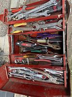 Overhead view inside the red toolbox showing an assortment of hand tools arranged in three compartments, including wrenches, pliers, and screwdrivers.