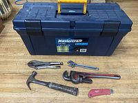 Photo showing the contents outside the tool box: locking pliers (vise grips), adjustable crescent wrench, pipe wrench with chipped jaw, claw hammer, and red utility knife