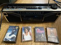Front view of GE boom box and 4 of the included cassette tapes showing album covers