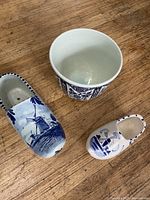 Photo of two Delft ceramic shoes and one Delft flower pot on wooden surface