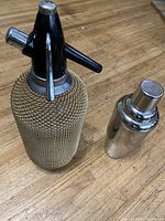 Seltzer bottle and cocktail shaker on wooden surface