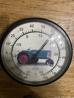 Front view of circular vintage thermometer with Oliver Model 80 tractor image and temperature scales.