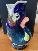 Side angle view of vintage WADE ceramic fish jug showing detailed colors and fish form, next to a black background.