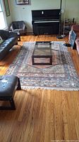 Living room rug under coffee table, piano, sofa and chair showing overall size, pattern and wear