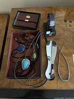Lot contents arranged on wooden surface including wallet, bolo ties, shoe horns, watch, and necklace