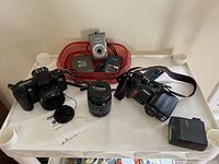 Overview of three cameras, extra lens, chargers in red tray