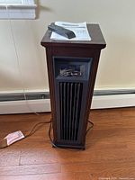 Tower heater standing on floor with power cord, remote and manual placed on top.
